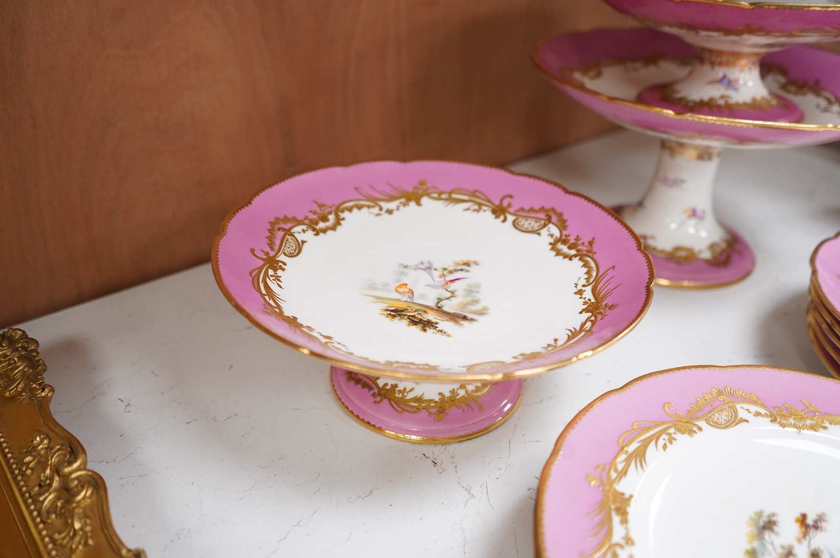 A Minton pink ground dessert service, in Sevres style, c.1850, hand painted with birds, comprising four comports and ten dessert plates, 23cm in diameter
